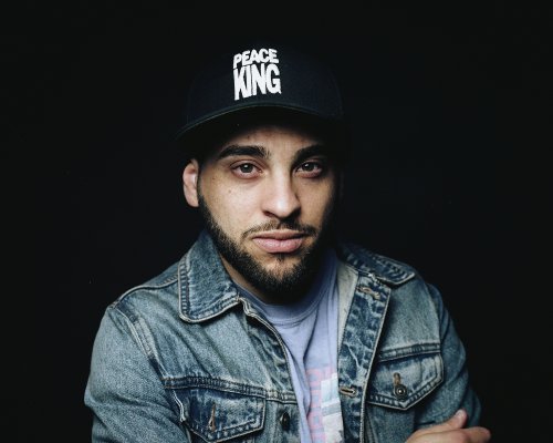Bearded man in denim jacket wearing black cap with PEACE KING sewn in white
