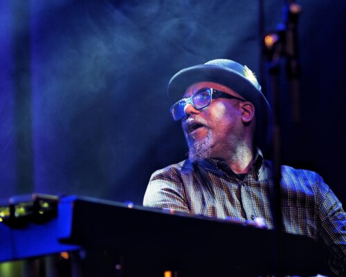 The artist, with bowler hat, playing keyboard in a stage setting