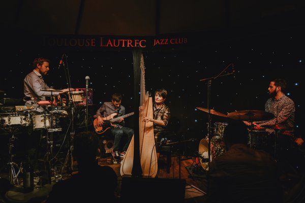 Three musicians surround Alina Bzhezhinska, who plays her harp in a warm club setting, sitting in front of starry lights.