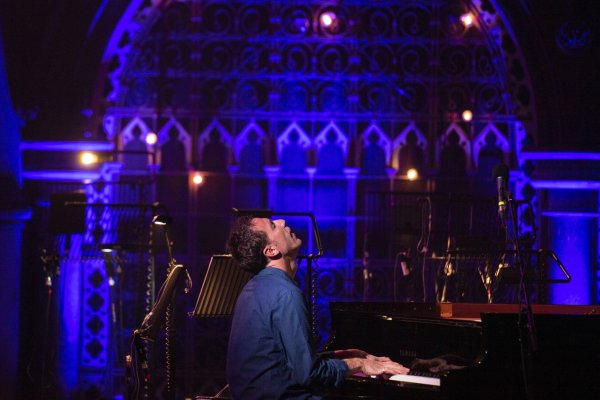 Bill Laurance sits at his piano with his head thrust back, in front of a magical lit-up chapel backdrop.