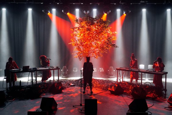 Silhouetted figures on stage with tree in background lit by dramatic red light