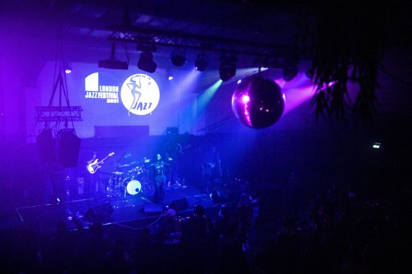 A band performs in a large club with a disco ball, lit by blue and purple lights.