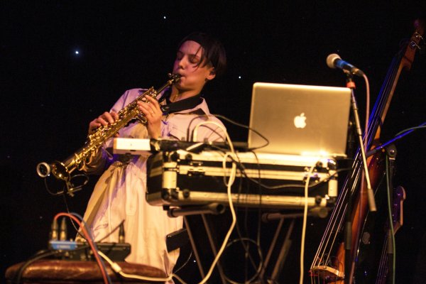 A close-up of a performer playing a soprano saxophone in front of a laptop desk