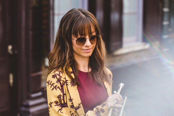 Yazz Ahmed, in a street, holding saxophone, wearing sunglasses
